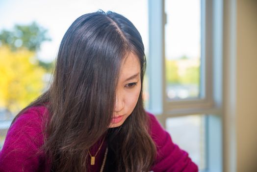 Sad looking young woman in front of a large window