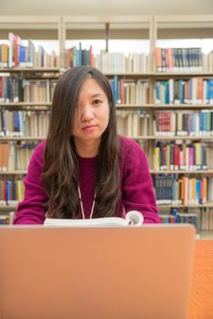 Woman with book and laptob studying in library