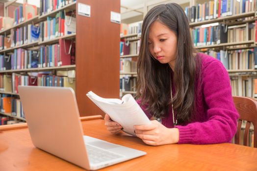 Woman with book and laptob studying in library