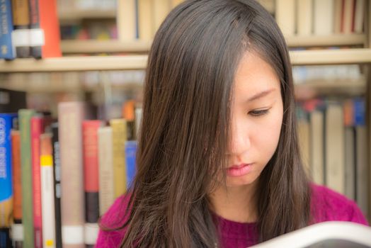 Woman reading a book next to a book shelf in library