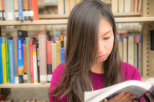 Woman reading a book next to a book shelf in library