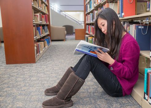 Woman reading a book next to a book shelf in library