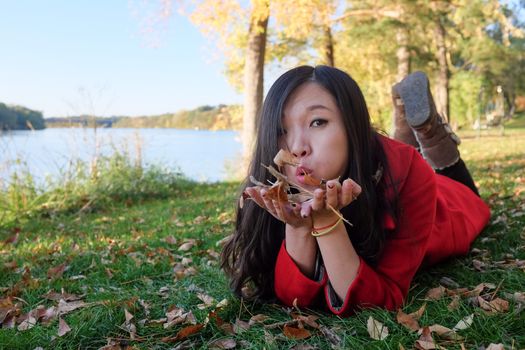 Woman laying on grass blowing away a handful of leaves