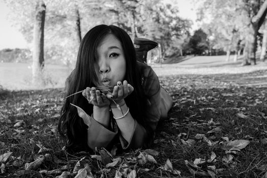 Woman laying on grass blowing away a handful of leaves