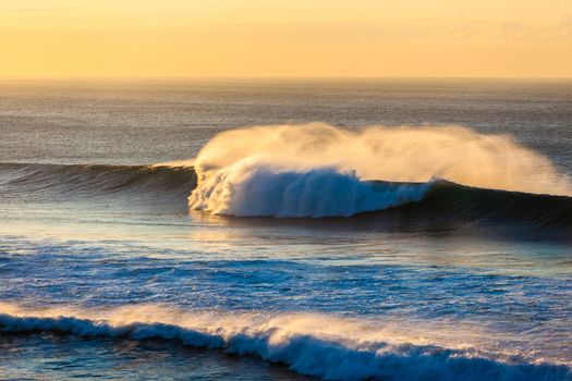 Ocean wave crashing breaking onto shallow shoreline reefs with offshore wind spray.