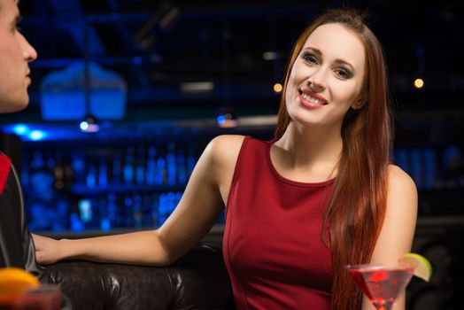 Portrait of an attractive woman in a nightclub, sitting on the couch with a drink