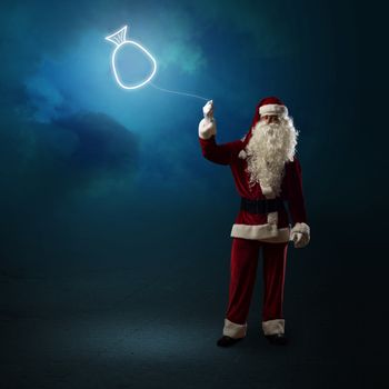 Santa Claus is holding a shining symbol of the bag with gifts on a string