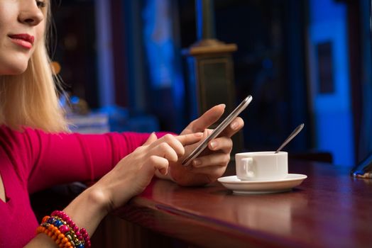 close-up of female hands holding a cell phone, sitting at the bar, next to a cup of coffee