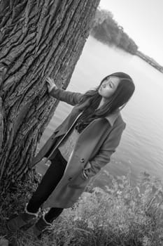 Portrait of young woman leaning against a tree next to a river