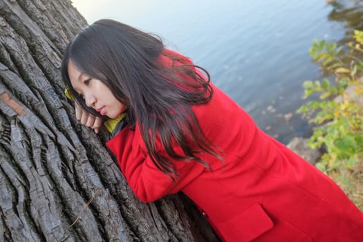 Portrait of young woman leaning against a tree next to a river