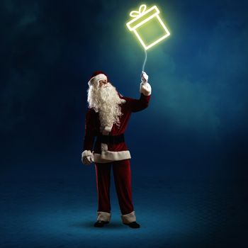 Santa Claus is holding a shining symbol of the gift on a string