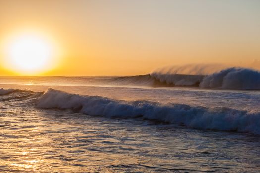 Large ocean waves breaking crashing towards the shoreline at sunrise.