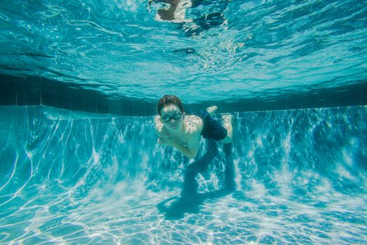 Young boy wearing goggles underwater in swimming pool.