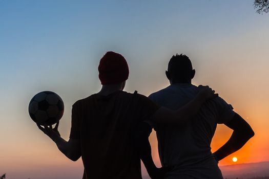 Friends body outlines silhouetted watch sunset after playing football.