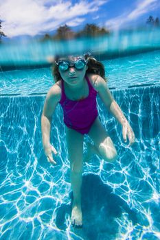 Young girl wearing goggles underwater in swimming pool.