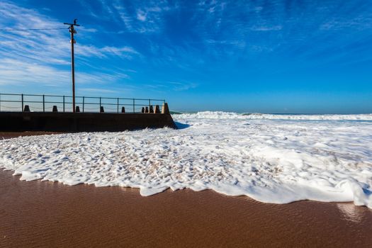 large ocean waves swells crashing breaking  and washing surging power around tidal pool beach sands.