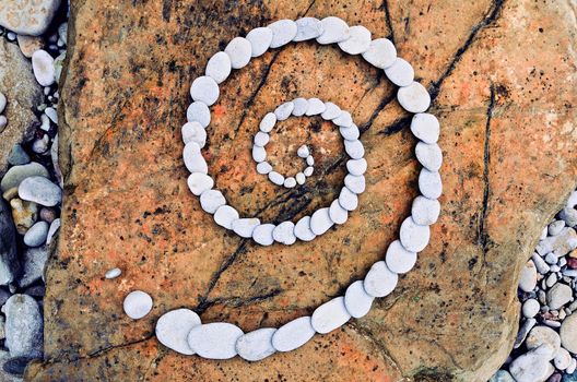 Spiral of white pebbles on the top of textured boulder