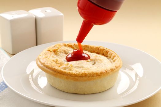 Tomato sauce being squeezed onto the classic Australian meat pie.