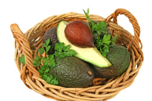 An avocado quarter with seed in a basket with avocados and parsley.