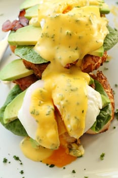 Delicious eggs benedict with hollandaise sauce with avocado with egg yolk.