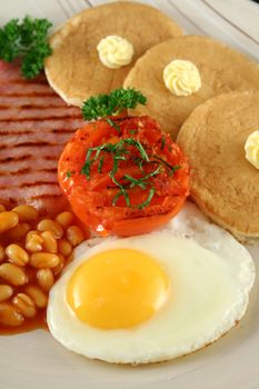 Breakfast of grilled bacon, tomato, egg, baked beans and pancakes.