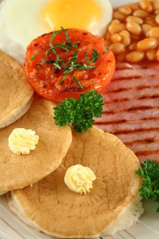 Breakfast of grilled bacon, tomato, egg, baked beans and pancakes.