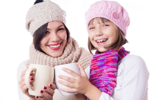 Happy mother and daughter in knitted hats with hot beverages over white