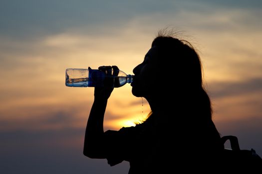 Black silhouette of girl drinking water in the ocean