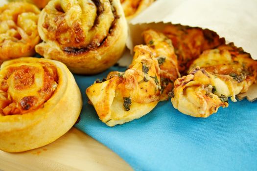 A selection of baked treats including tomato and herb sticks in a paper bag and baked scrolls.