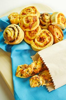 A selection of baked treats including tomato and herb sticks in a paper bag and baked scrolls.