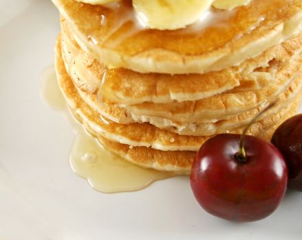 Honey syrup dripping down hot pancakes with cherries.