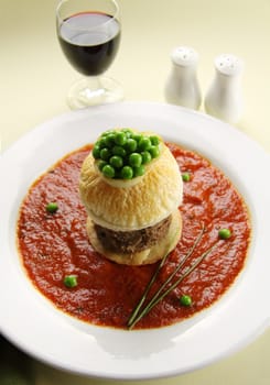 Tall beef pie with peas floating in tomato sauce.