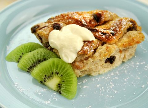 Delicious bread and butter pudding dessert with kiwi fruit and cream.