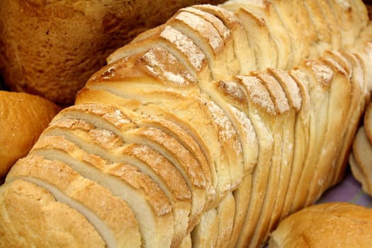 Background of loaf of fresh baked sliced bread amongst other types of bread.