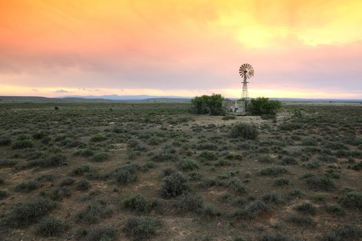 Wide open farm land with a water windmill pump at sunset in the Karoo in South Africa