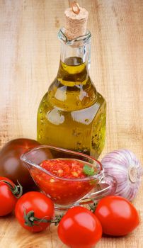 Arrangement of Bruschetta Sauce in Glass Gravy Boat with Tomatoes, Garlic and Olive Oil in Glass Bottle closeup on Wooden background