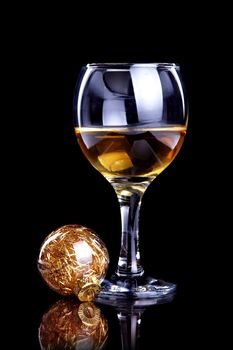 Glass with drink and a Christmas ball on a black background. Glass with alcohol and a Christmas ball.