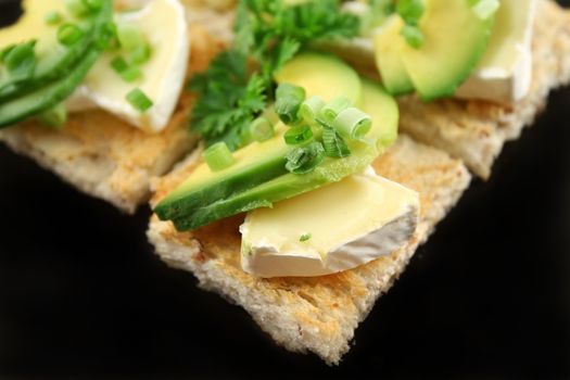 Camembert and avocado bites with spring onions on wholegrain squares.