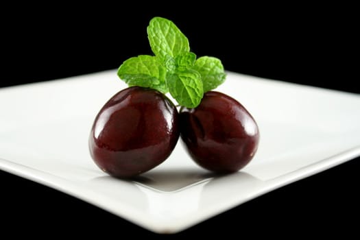 Two cherries on a plate with mint.