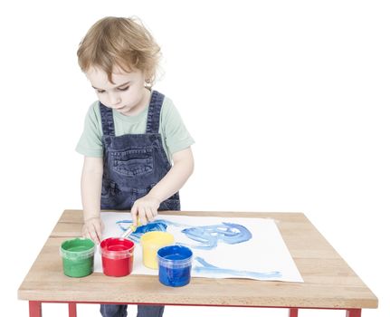 cute child making painting on small desk. studio shot isolated on white background