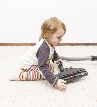 young child sitting next to vacuum cleaner