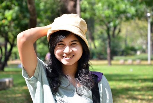 Portrait of beautiful smiling young woman in yellow hat, against background of summer green park