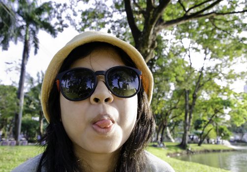 Young naughty woman in yellow cap looking at camera through sunglasses and sticking out tongue