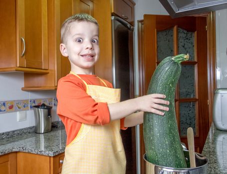 Cute child chef with apron cooking big zucchini and other vegetables in a pot on the kitchen