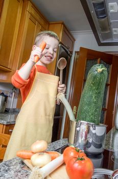 Cute child chef with apron cooking big zucchini and other vegetables in a pot on the kitchen