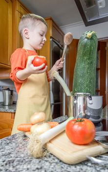 Cute child chef with apron cooking big zucchini and other vegetables in a pot on the kitchen