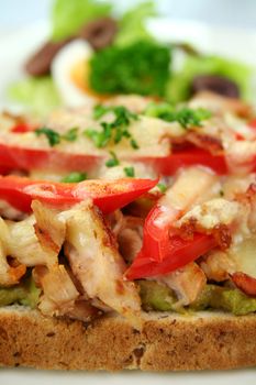 Grilled open chicken sandwich with avocado, peppers and cheese with a side salad.