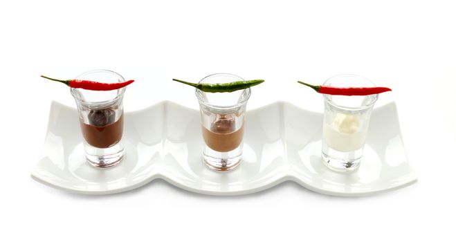 A row of red and green hot chillies lined up in shot glasses with dark, white and milk chocolate.