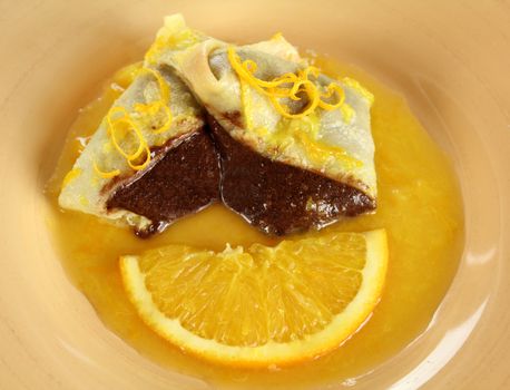 Sliced chocolate crepe suzette with orange sauce and a slice of orange.