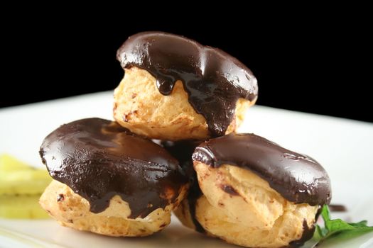 Stack of chocolate profiteroles with kiwi fruit on a plate.